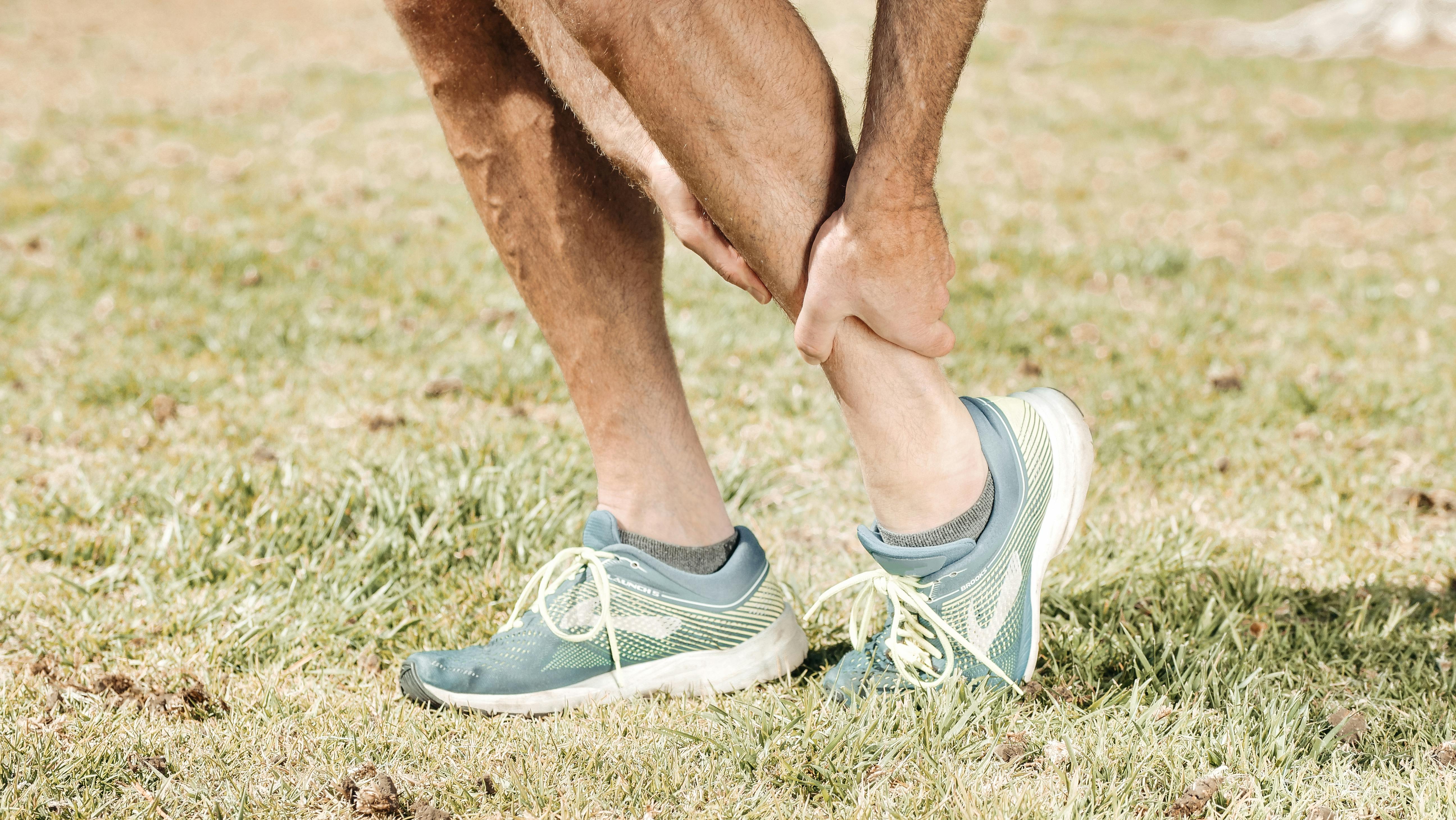 Man holding his calf in pain, wearing teal sneakers on green grass